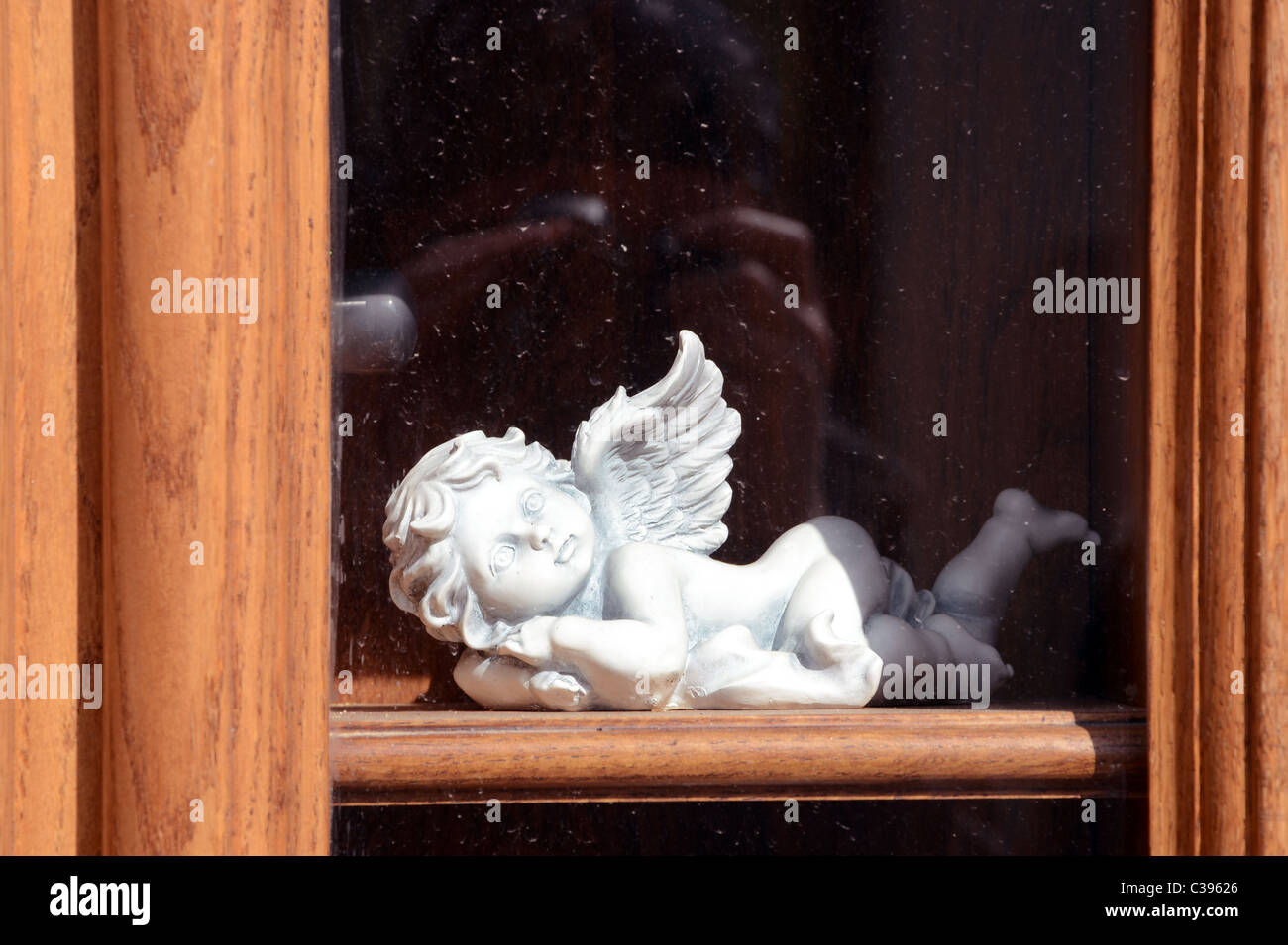 Bianco di ceramica angelo sulla finestra in legno davanzale dietro il vetro. Foto Stock