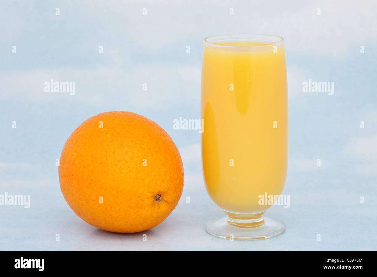 Un bicchiere di succo d'arancia fresco con un tutta arancione contenenti vitamina C contro un cielo blu sullo sfondo Foto Stock