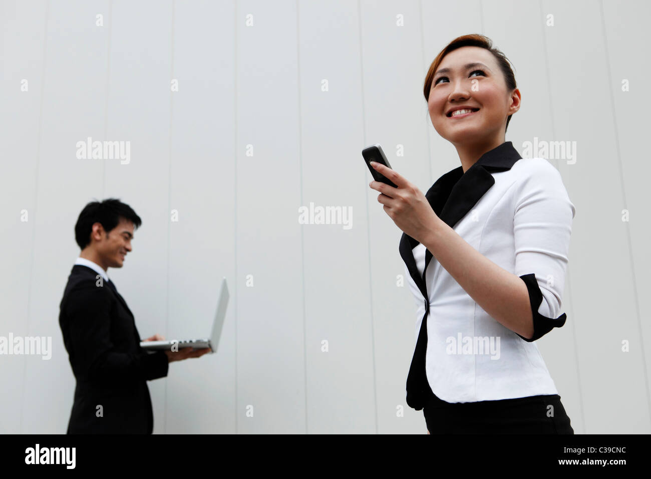 Donna che mantiene la mano telefono mentre l'uomo utilizza lap top in massa posteriore Foto Stock