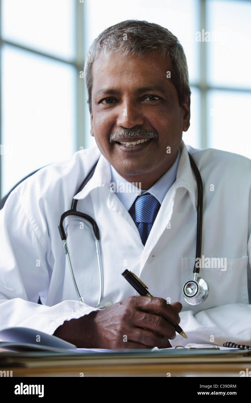 Medico indiano seduto alla scrivania e sorridente Foto Stock