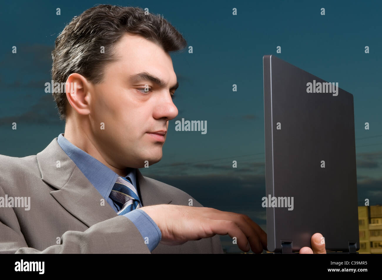 Uomo in una tuta contro il cielo di sera con il computer portatile Foto Stock