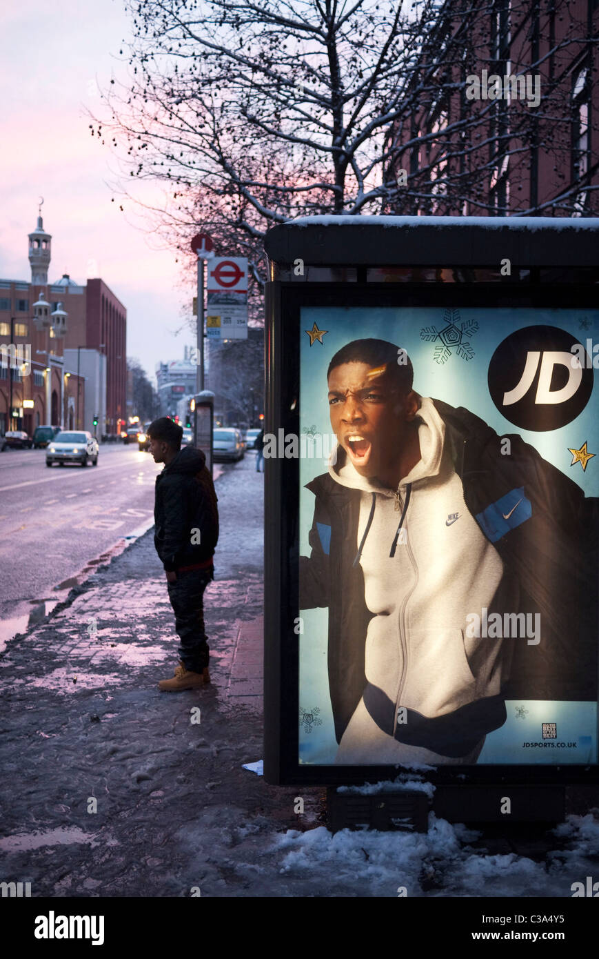 La pubblicità a una fermata degli autobus in Whitechapel High Street. Un giovani asiatici attende accanto a un poster che sembra essere grida a lui. Foto Stock