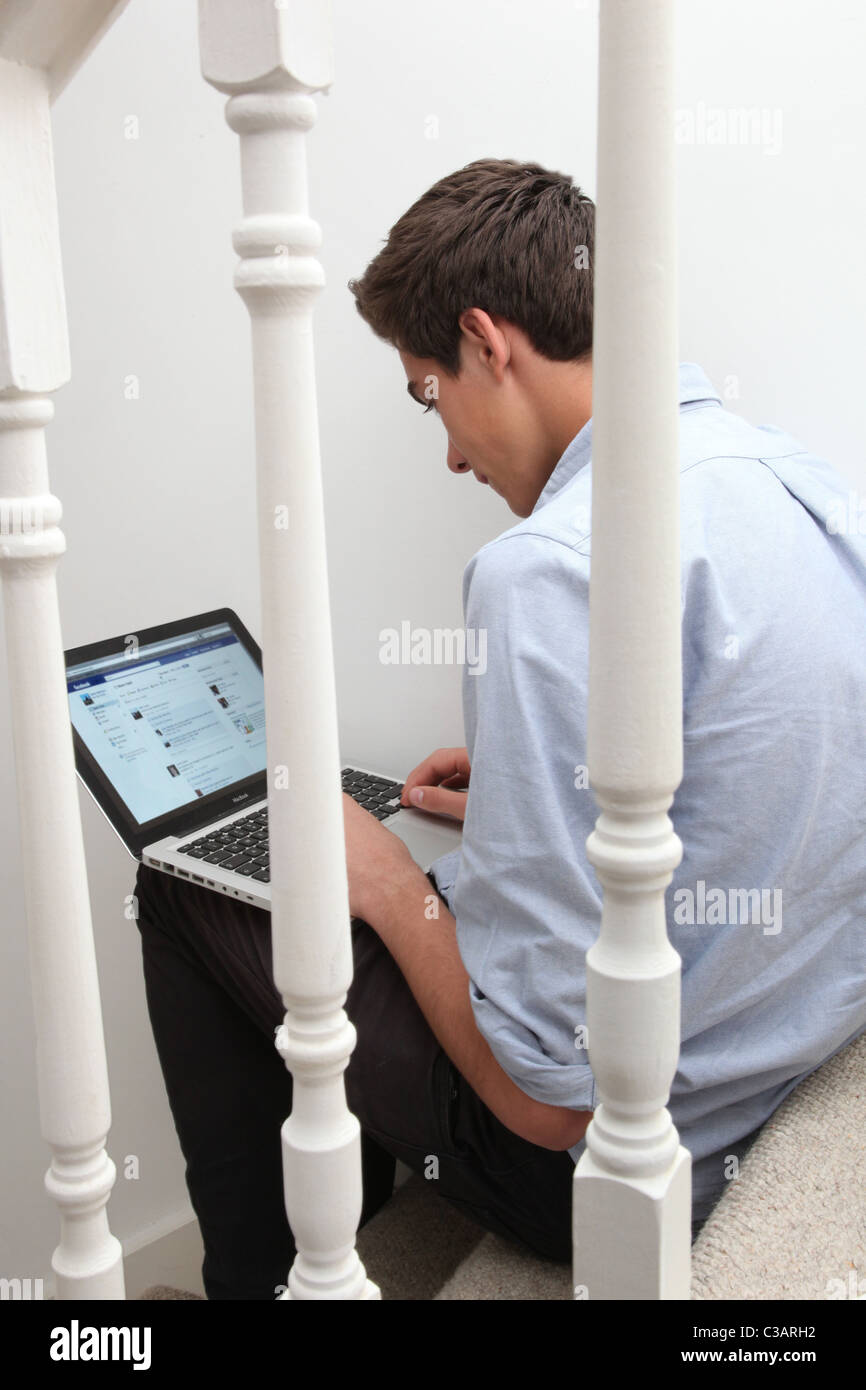 Giovane maschio seduto da solo su per le scale con il suo computer portatile guardando facebook Foto Stock