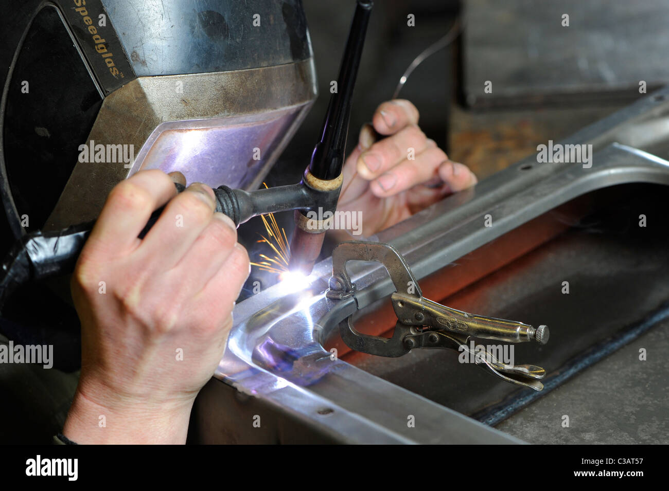 Un esperto lavoratore di metallo a lavorazione dei metalli, mediante saldatura TIG metodo per effettuare una riparazione su un VW camper porta. Foto Stock