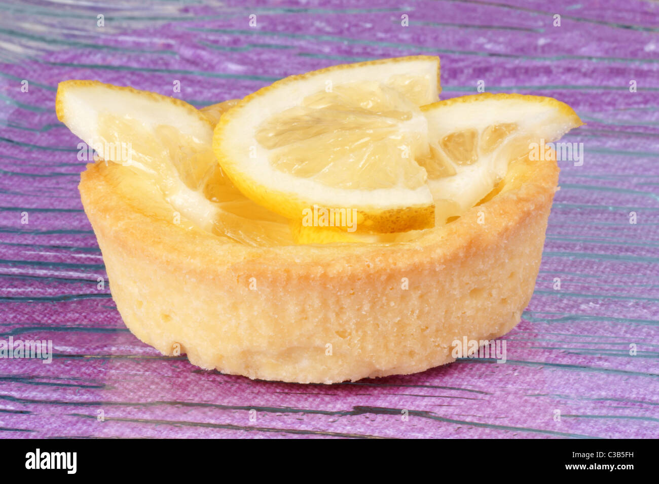Primo piano di una mini limone crostata di frutta su una lastra di vetro su uno sfondo di colore rosa. Con copy-spazio. Messa a fuoco selettiva. Foto Stock