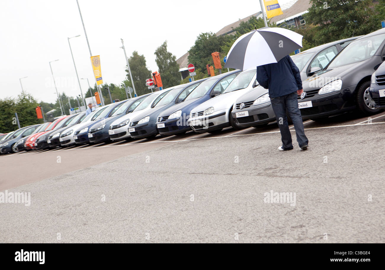 Un uomo che porta un ombrello passeggiate dopo una fila di automobili per la vendita di Cambridge. Foto Stock
