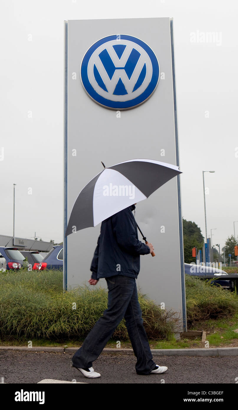 Un uomo che porta un ombrello passeggiate passato un segno di Volkswagen, Cambridge. Foto Stock