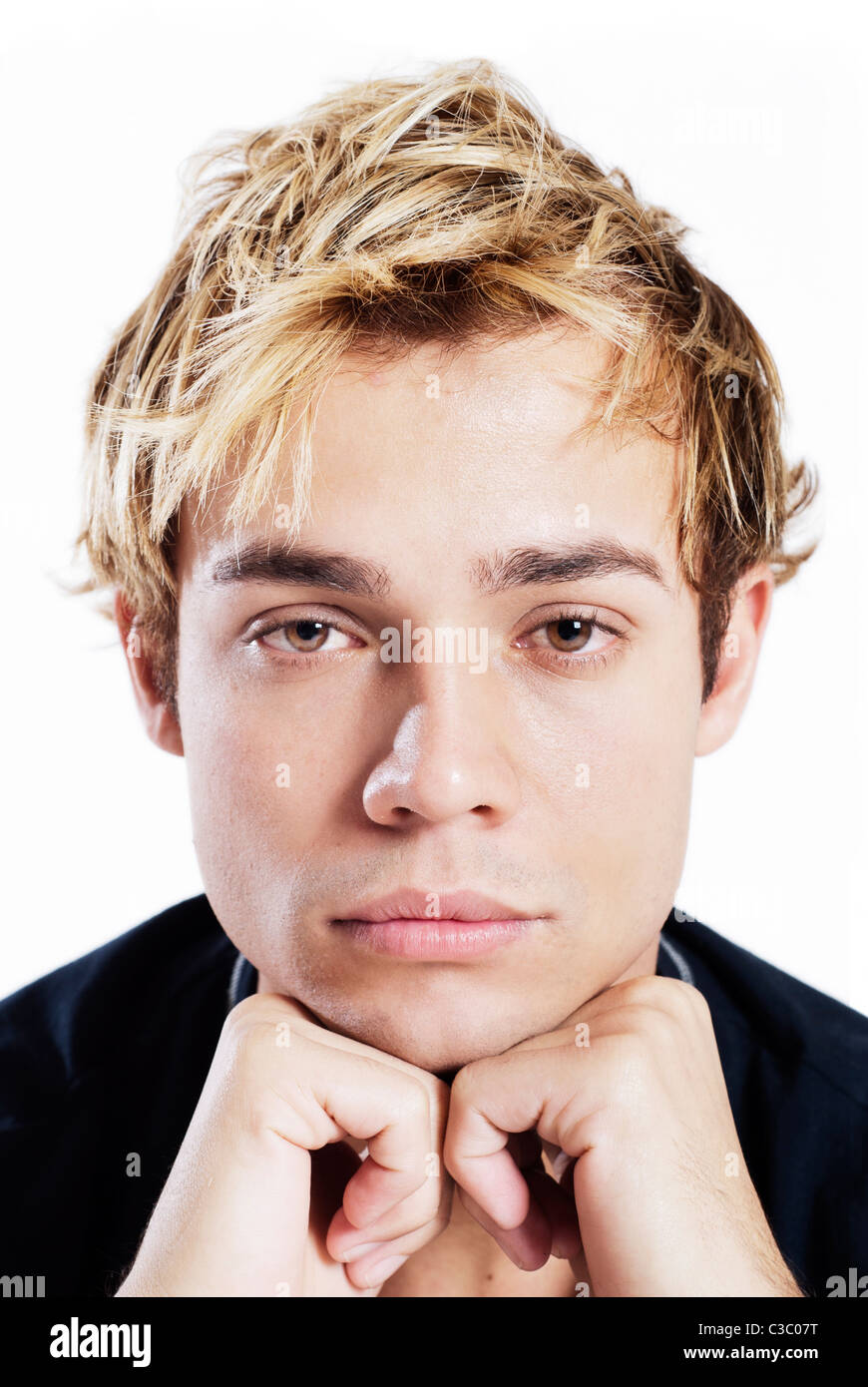 Ritratto di un giovane maschio adulto in camicia nera come si siede con le mani sul mento Foto Stock