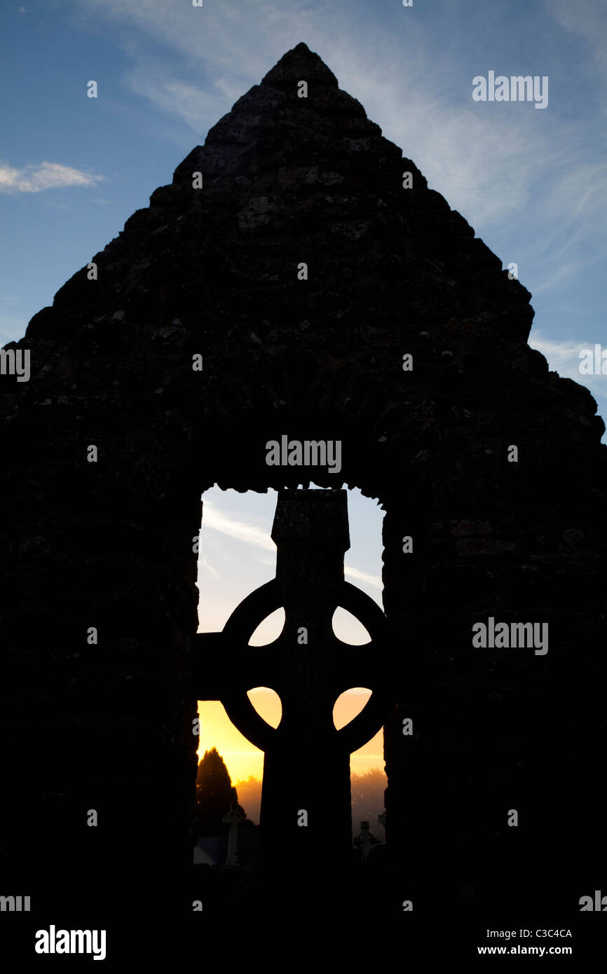 Croce celtica e tempio profilarsi all'alba, Monastero di Clonmacnoise, nella contea di Offaly, Irlanda. Foto Stock