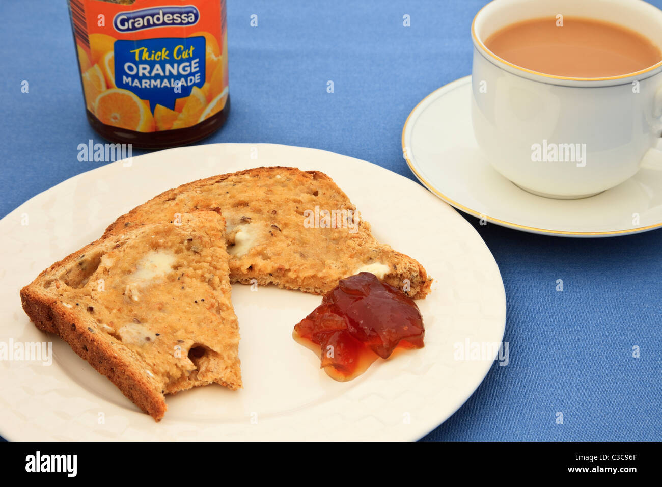 Una fetta di in parte imburrata mangiato pane tostato con un vasetto di marmellata e una tazza di tè su un piattino su una tovaglia blu. Regno Unito Foto Stock