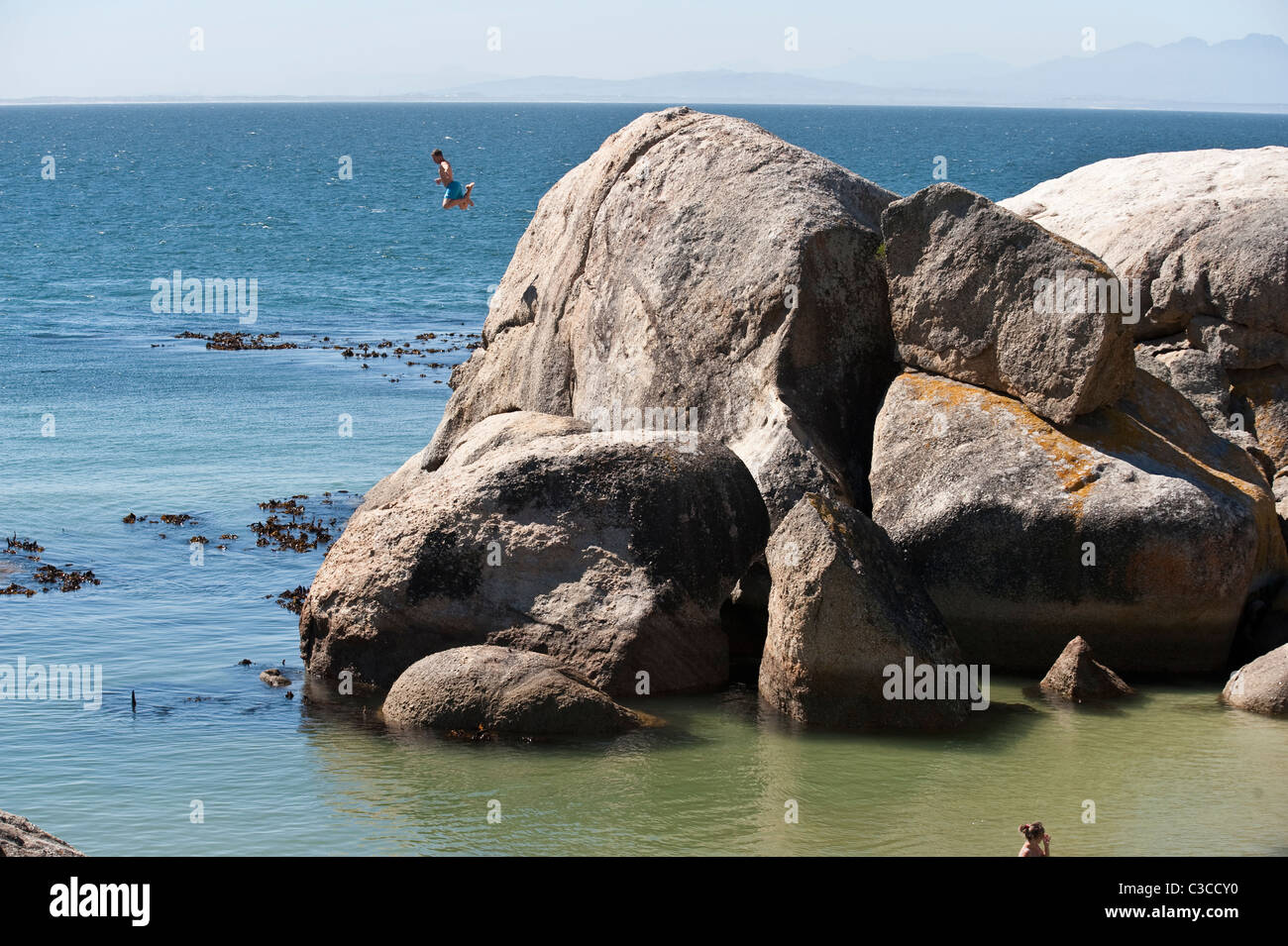 L'uomo jumping al mare dalla roccia di granito Boulders Beach Città di Simon Table Mountain NP Penisola del Capo Western Cape Sudafrica Foto Stock