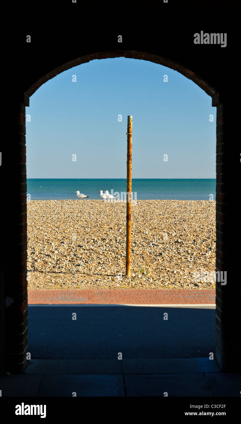 Worthing beach con i gabbiani e un arrugginito pole shot attraverso un arco scuro, worthing sussex, Regno Unito Foto Stock