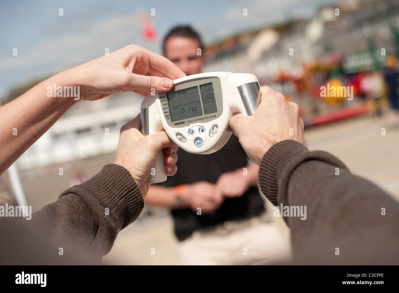 Una persona avente un libero checkup usando un OMRON tenuto in mano il grasso corporeo monitor Foto Stock