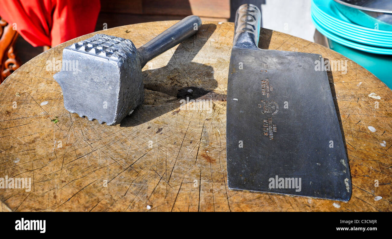 Un vecchio tenerizzazione della carne un martello e una carne cleaver sedersi su un vuoto di legno rotondo blocco di trinciatura, che aspetta solo di essere utilizzato. Foto Stock