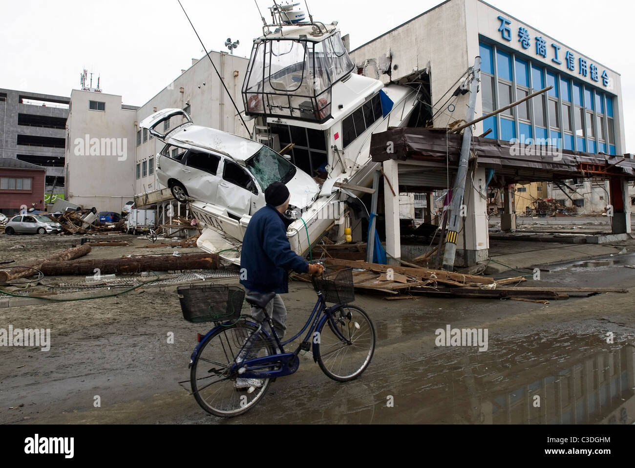 Un uomo spinge la sua bicicletta passato uno yacht che è stato forzato in un edificio dalla forza del marzo 11 dallo tsunami di Ishinomaki, Giappone Foto Stock