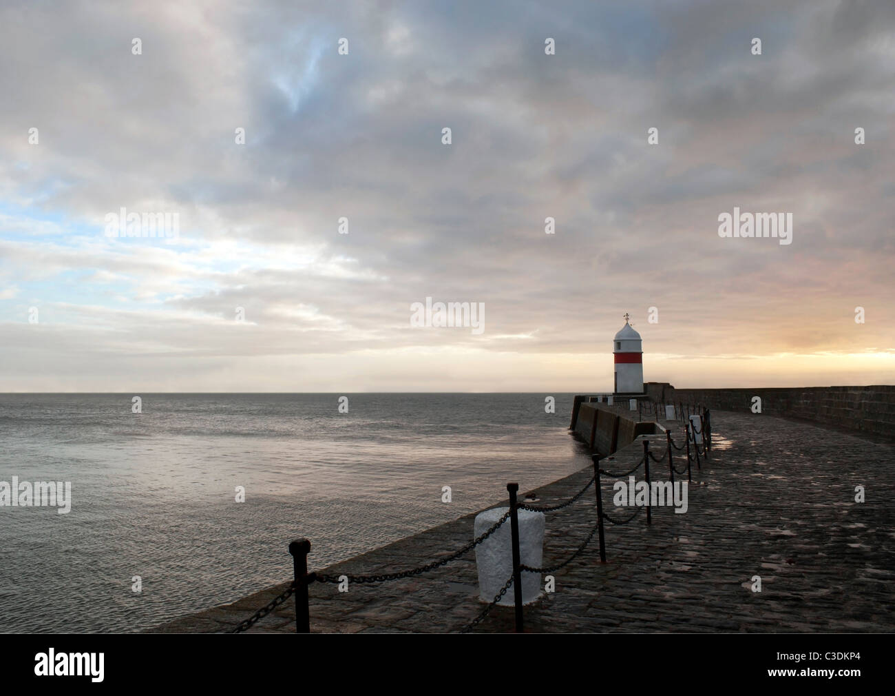 Percorso al faro sul muro frangiflutti con drammatica cielo e mare calmo all'alba Foto Stock