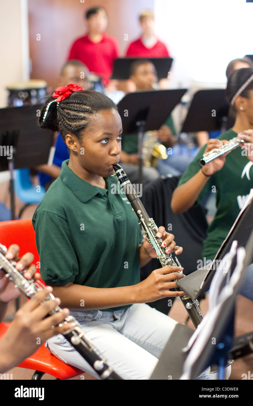 Femmina afro-americano di alta scuola studente legge spartiti di musica e suona il clarinetto durante la pratica di banda nella banda hall. Foto Stock