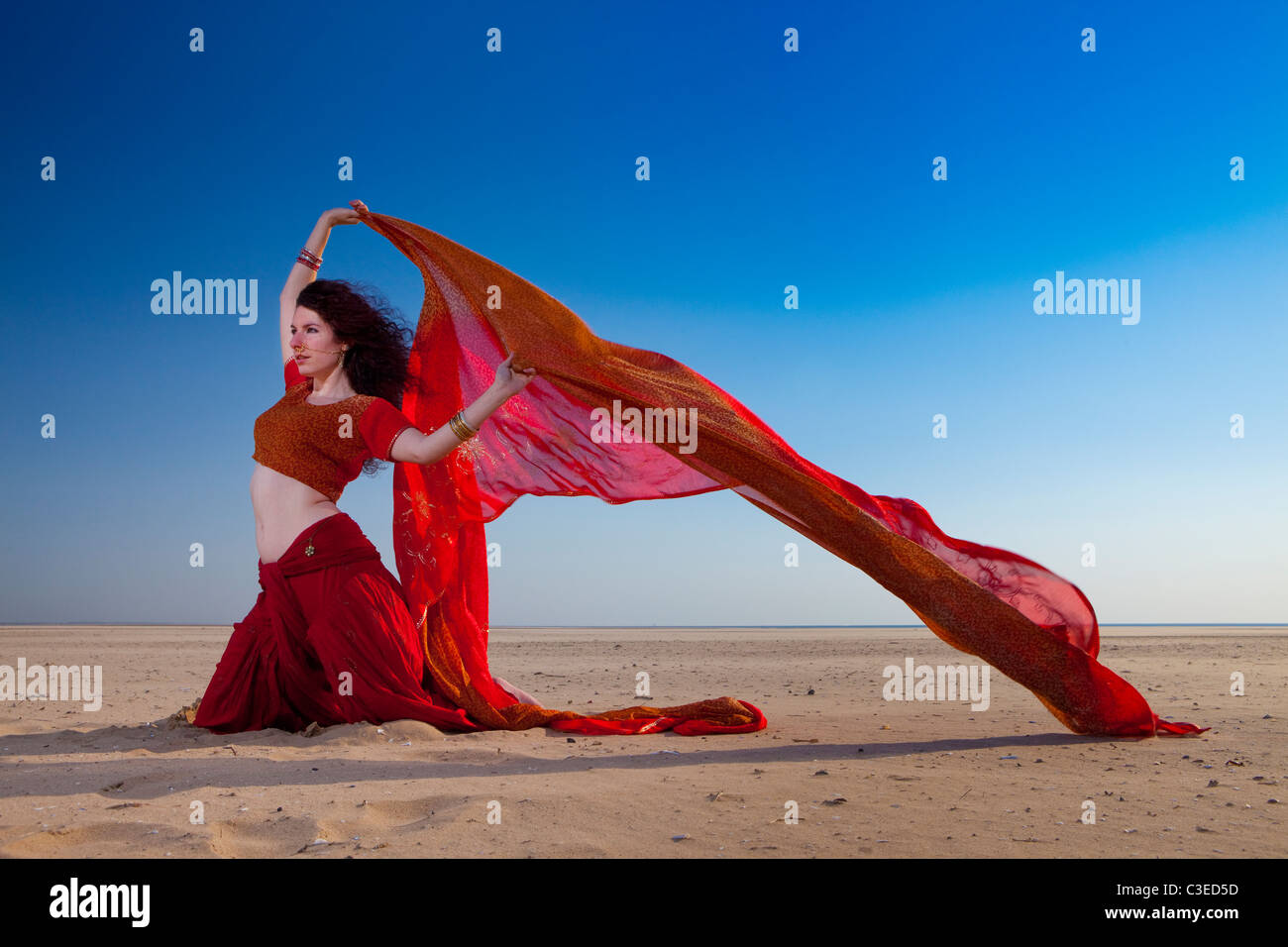 Giovane e bella "danzatrice del ventre' pongono gli scioperi contro il cielo drammatico e la spiaggia in abbigliamento indiano, UK. Bellydancer e yoga Foto Stock