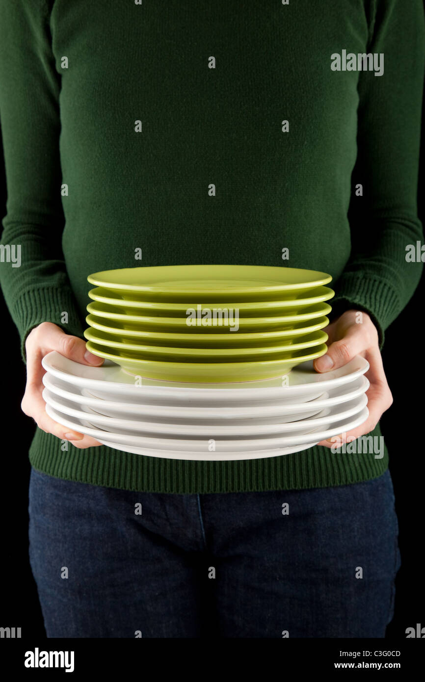 Mani femminili tenendo un mucchio di verde e piatti bianchi Foto Stock