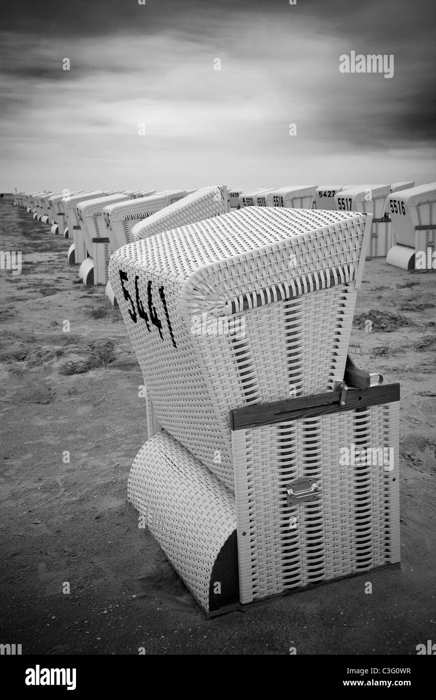 Righe di abbandonato coperto e sedie da spiaggia in vimini in una spiaggia in bianco e nero Foto Stock