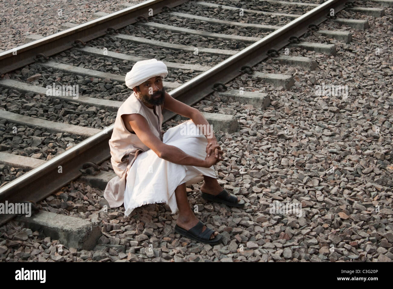 Uomo seduto vicino a binari ferroviari, Ahmedabad, Gujarat, India Foto Stock