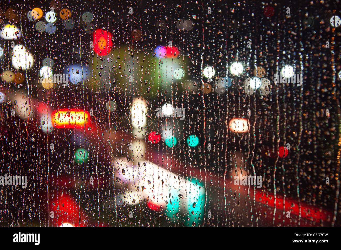 Fari di automobili, i semafori e le aziende come visto attraverso una pioggia-opener finestra la notte Foto Stock