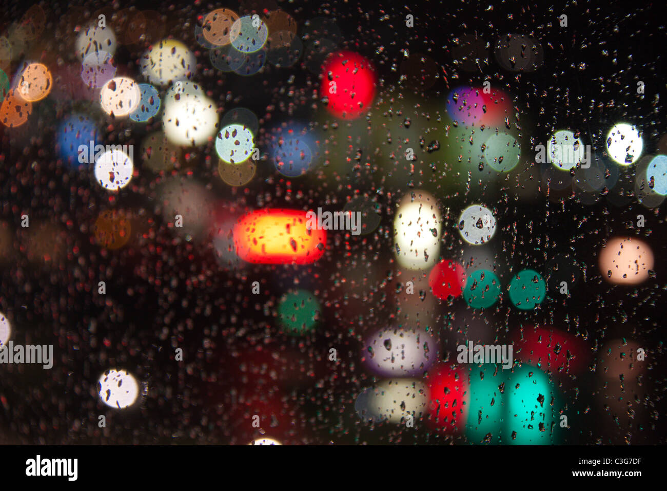 Fari di automobili, i semafori e le aziende come visto attraverso una pioggia-opener finestra la notte Foto Stock