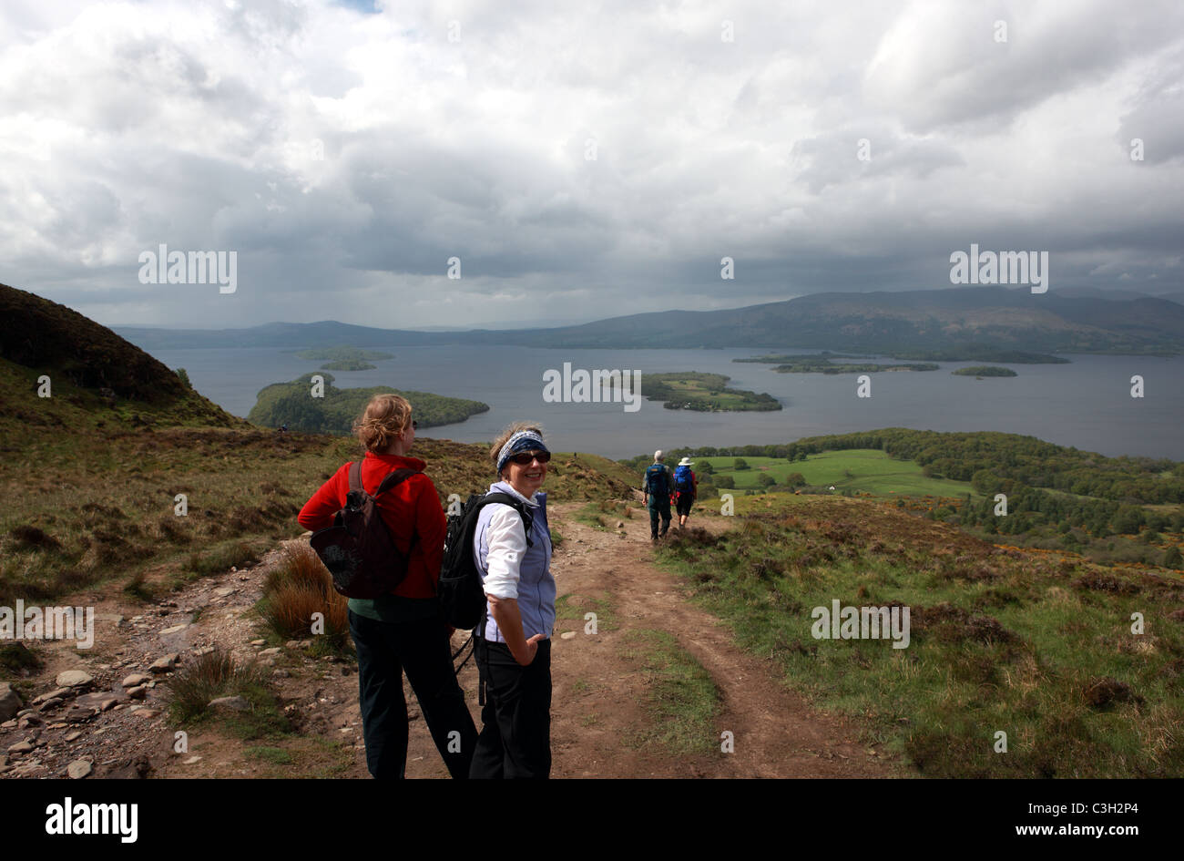 Walkers sul colle conico ammirando la vista sul Loch Lomond in Scozia Foto Stock