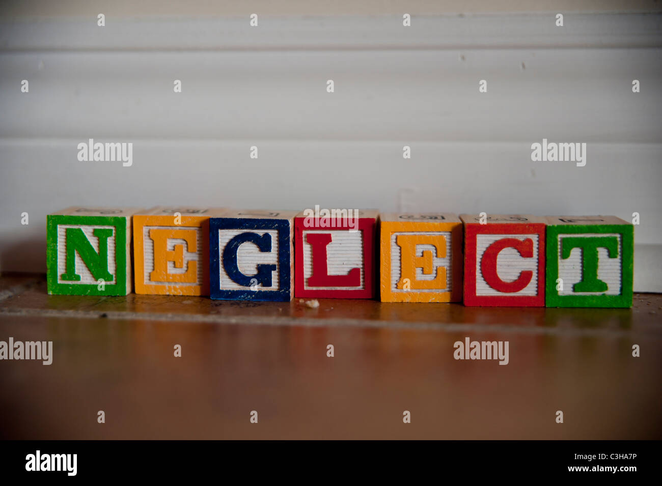 La parola abbandono enunciato in colorate per bambini lettere di blocco in un angolo polveroso di una casa. Foto Stock