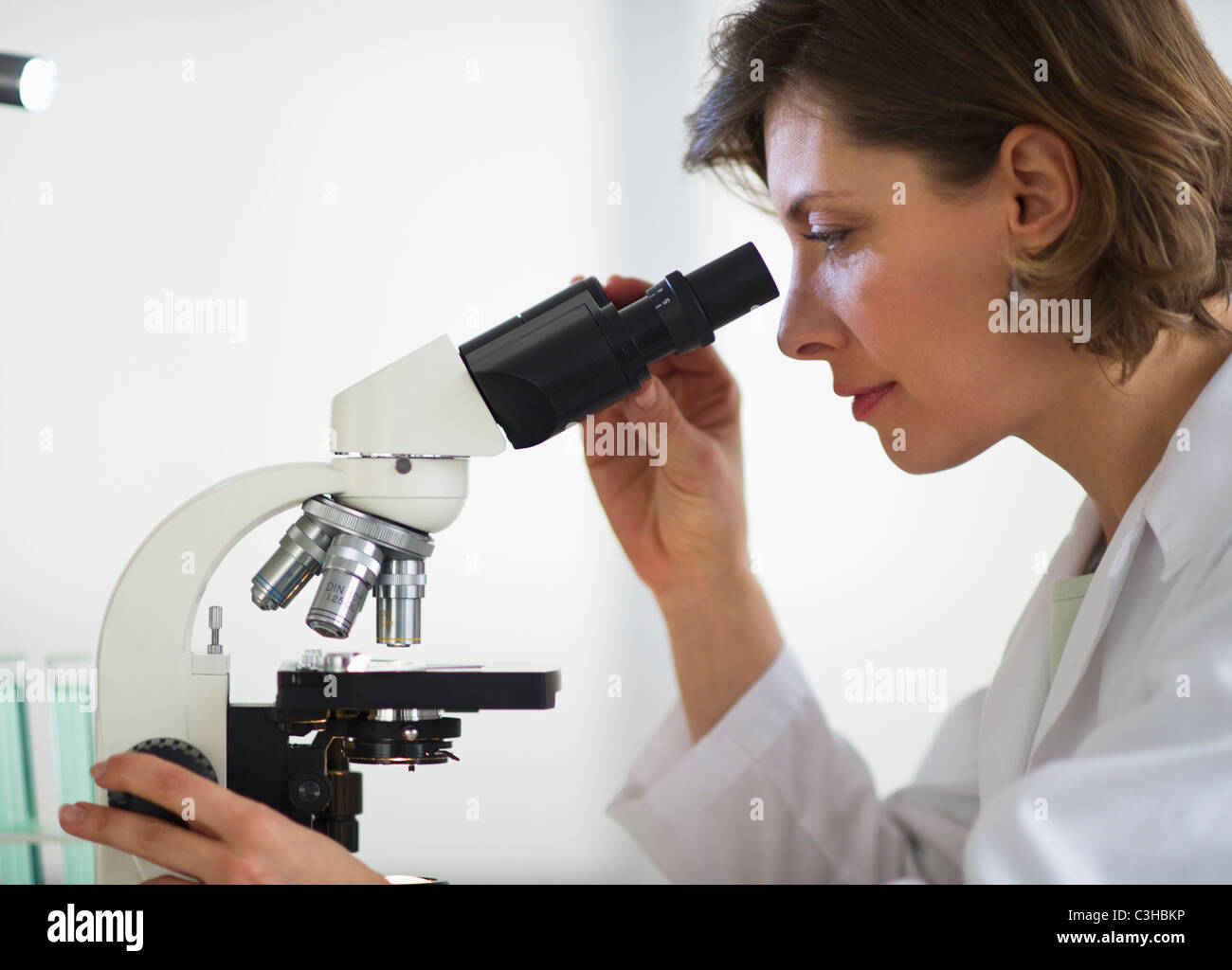 Donna nel laboratorio di ricerca attraverso il microscopio Foto Stock