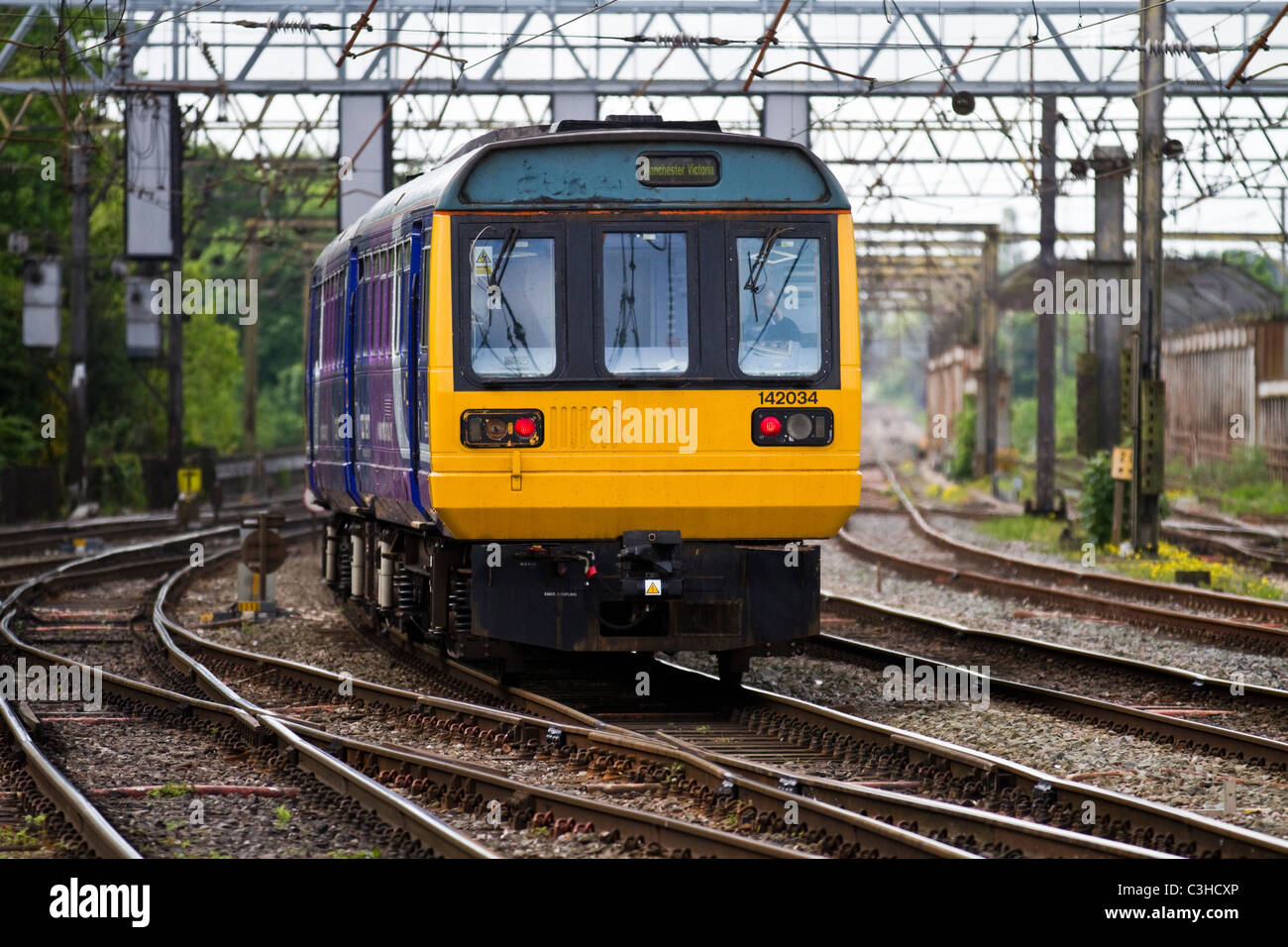 142034 " commuter " treno passeggeri, le linee di potenza & portali avvicinando Preston stazione ferroviaria, Lancashire, Regno Unito Foto Stock