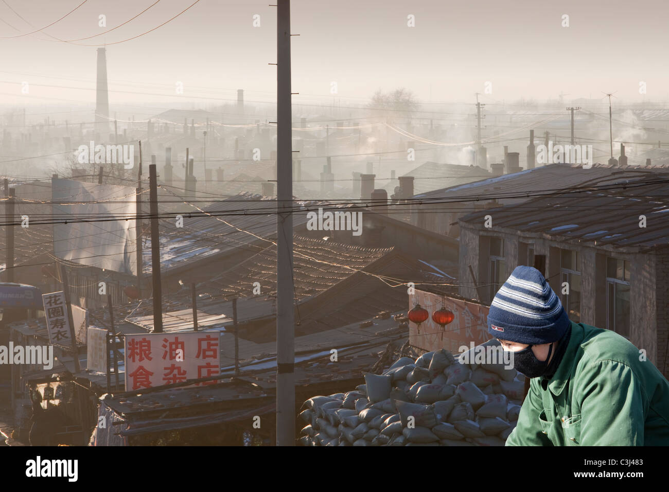 Le emissioni da carbone home incendi in Suihue,Cina con un ciclista che indossa una maschera di smog. Foto Stock