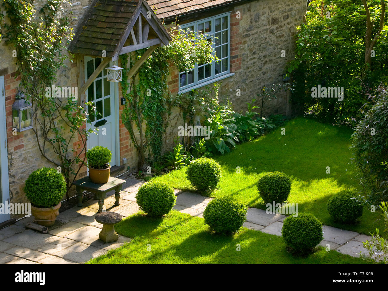 Percorso attraverso il prato bordato con topiaria da scatola che conduce al portico cottage in inglese giardino estivo Foto Stock