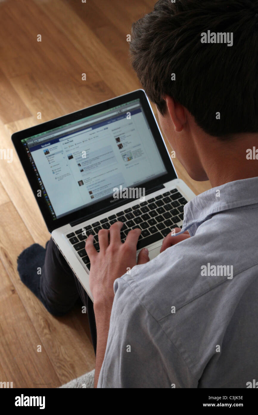 Giovane maschio con un computer portatile sulla pagina Facebook. Foto Stock