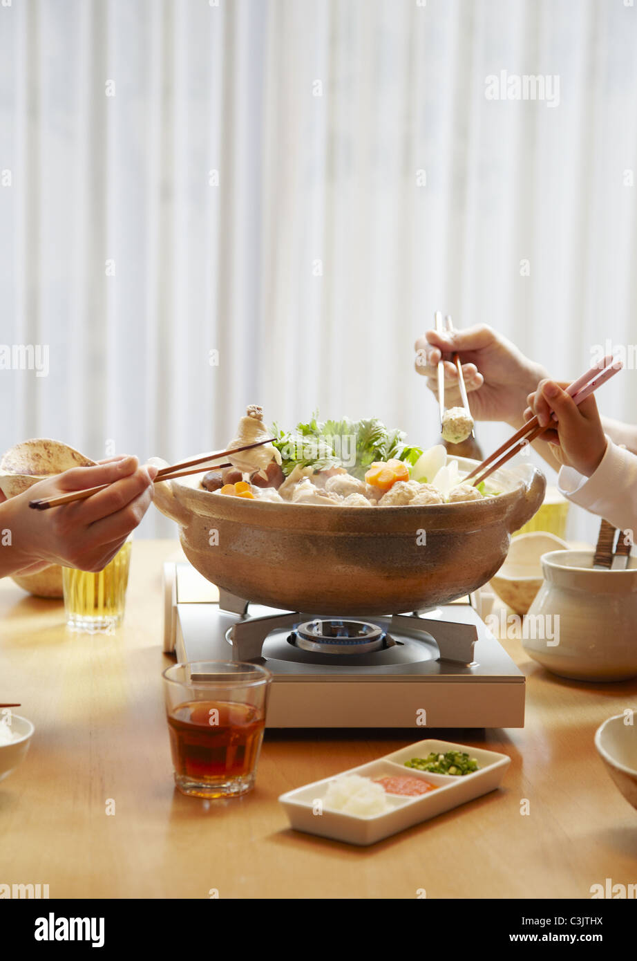 Famiglia con le mani in mano a mangiare giapponese hot pot Foto Stock