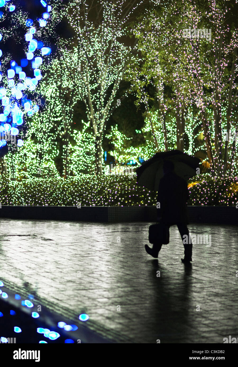 Silhouette di uomo a camminare con ombrello sotto gli alberi con indicatori verdi e blu Foto Stock