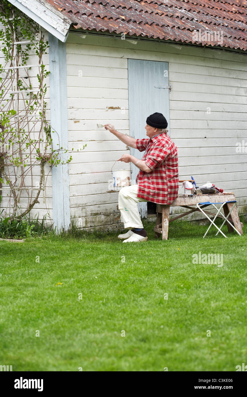 Uomo anziano dipinto il suo cottage estivi, Svezia. Foto Stock
