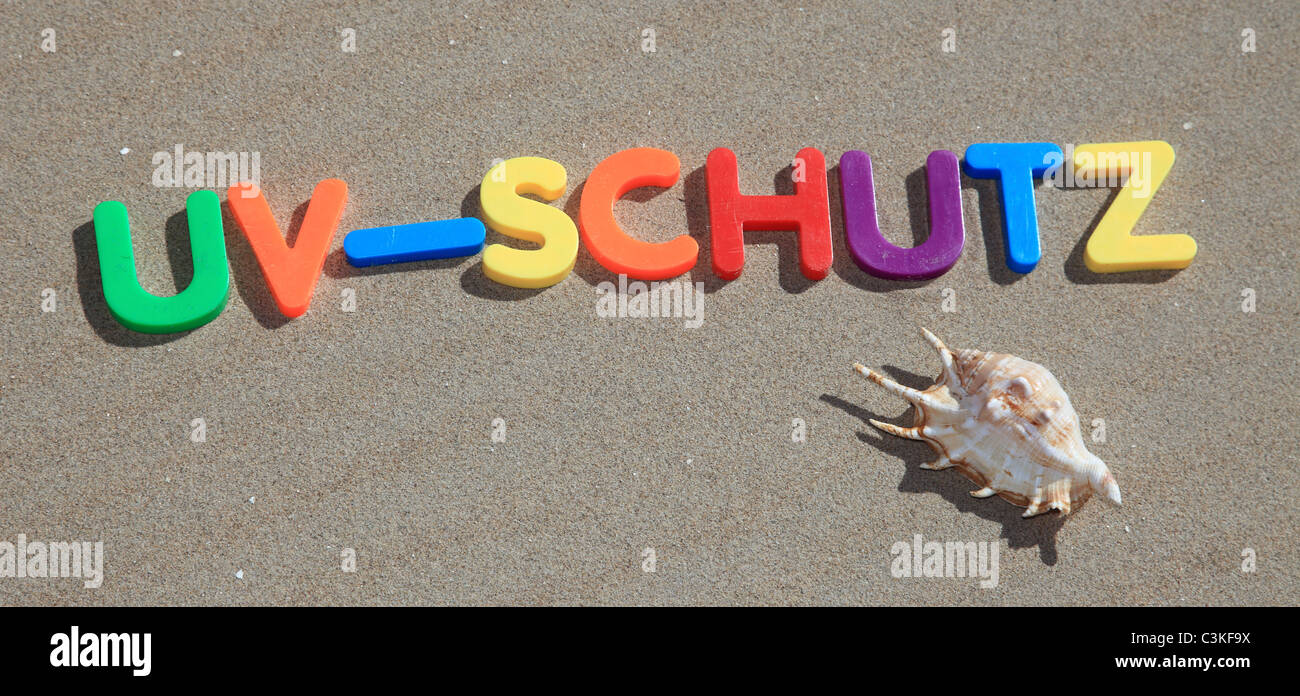 Il termine tedesco uv-schutz scritto in lettere colorate sulla sabbia. Foto Stock