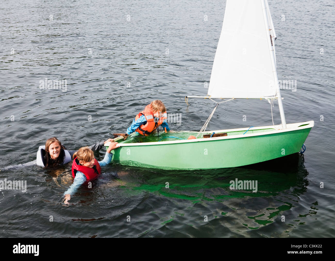 Tre bambini che cercano di entrare in gommone Foto Stock