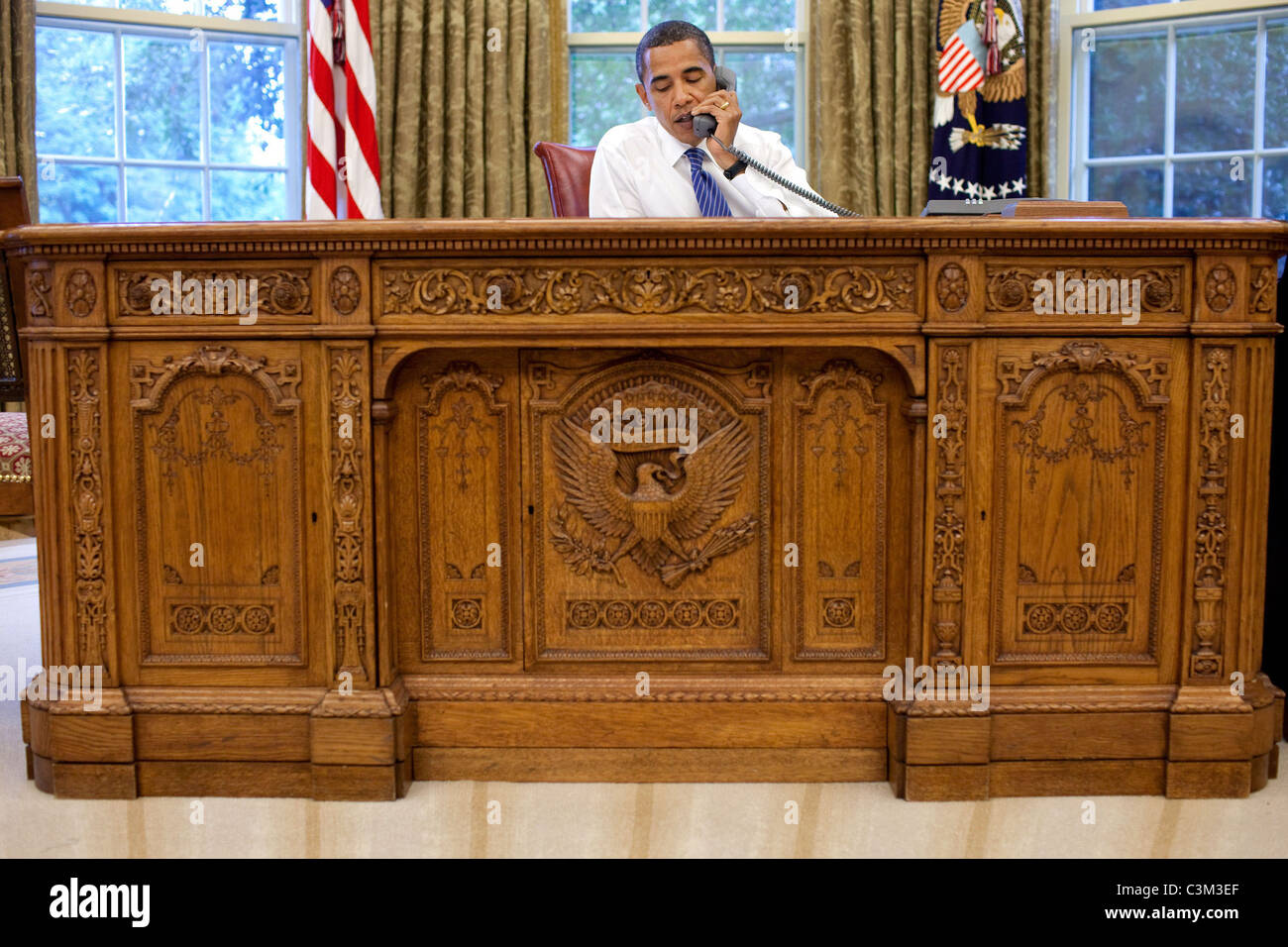 Il presidente Barack Obama si siede dietro la scrivania risoluto nell'Ufficio Ovale durante una chiamata in conferenza con persone di fede Foto Stock