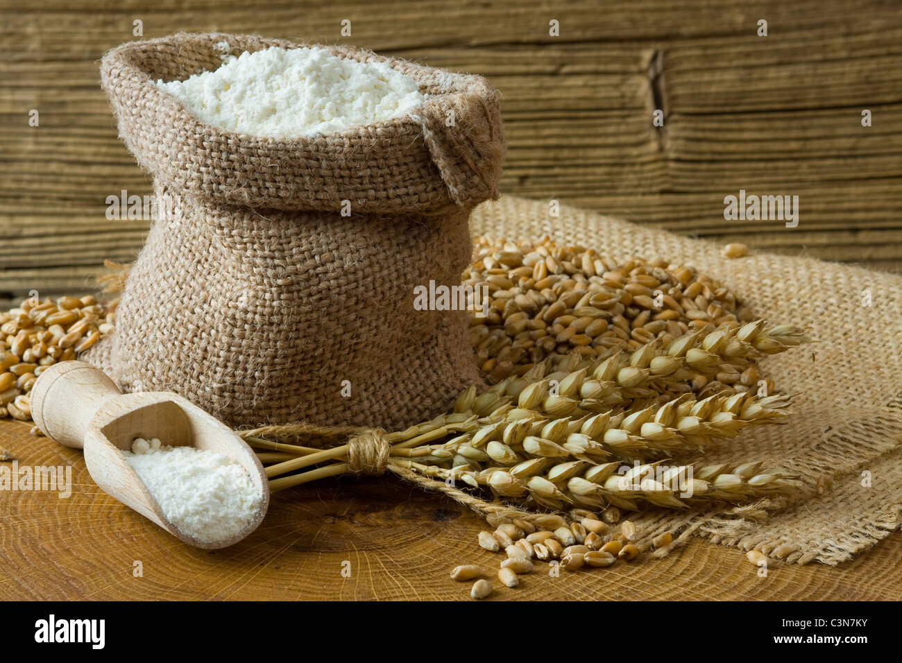 Chicco di grano e farina in piccolo sacchetto di tela su sfondo di legno Foto Stock