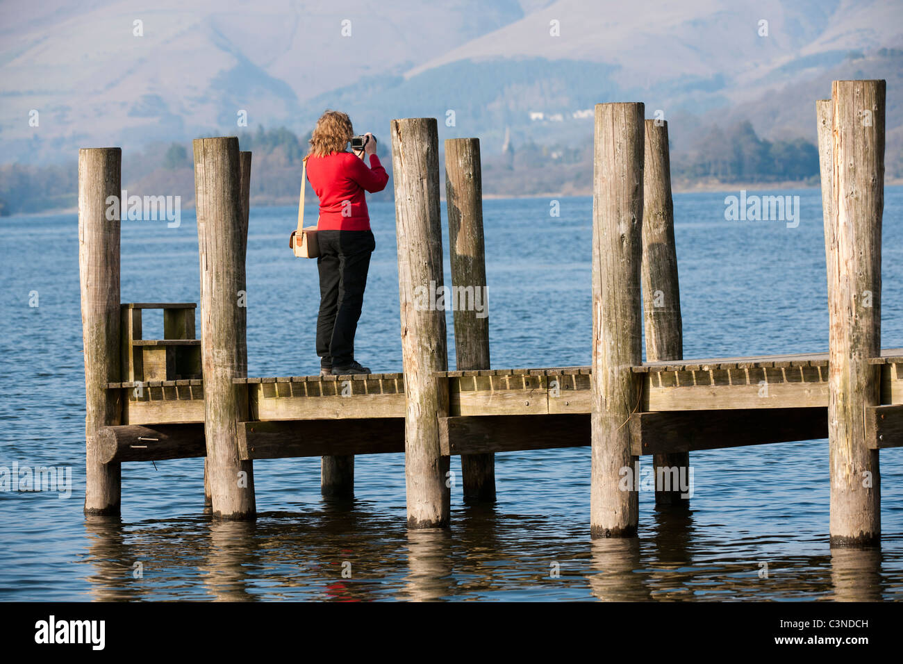 Donna fotografo scattare una fotografia da un pontile di sbarco sulla Derwent Water, Cumbria, England, Regno Unito Foto Stock