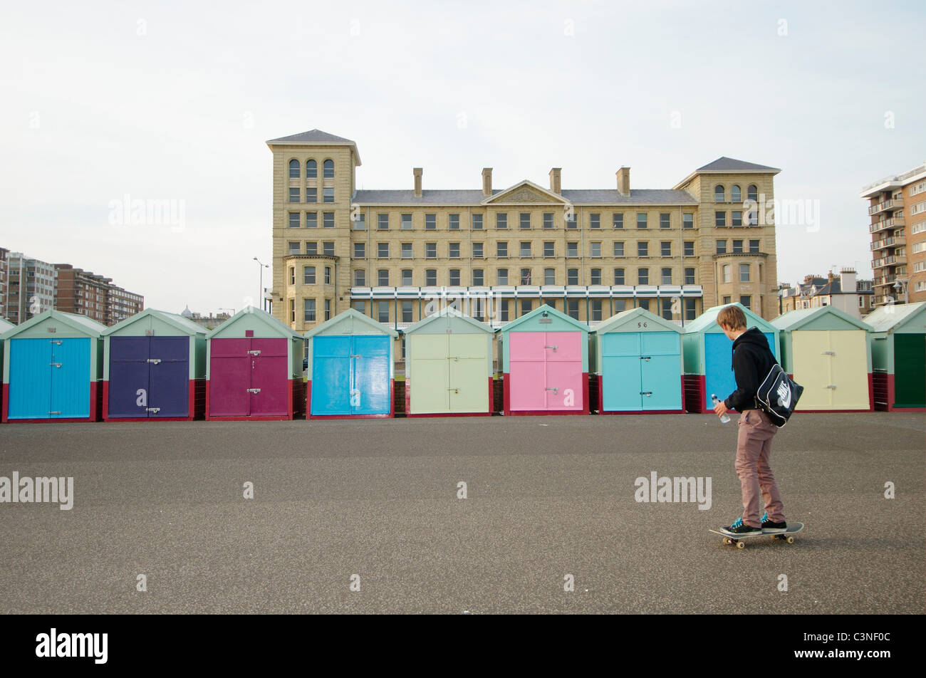 Giovane uomo skateboarding colorato passato cabine sulla spiaggia, sul lungomare di Brighton. Brighton, Regno Unito Foto Stock