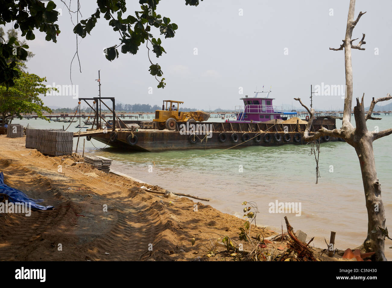 Una chiatta che trasportano materiali da costruzione essendo scaricato in Chalong Bay, Phuket Thailandia Foto Stock