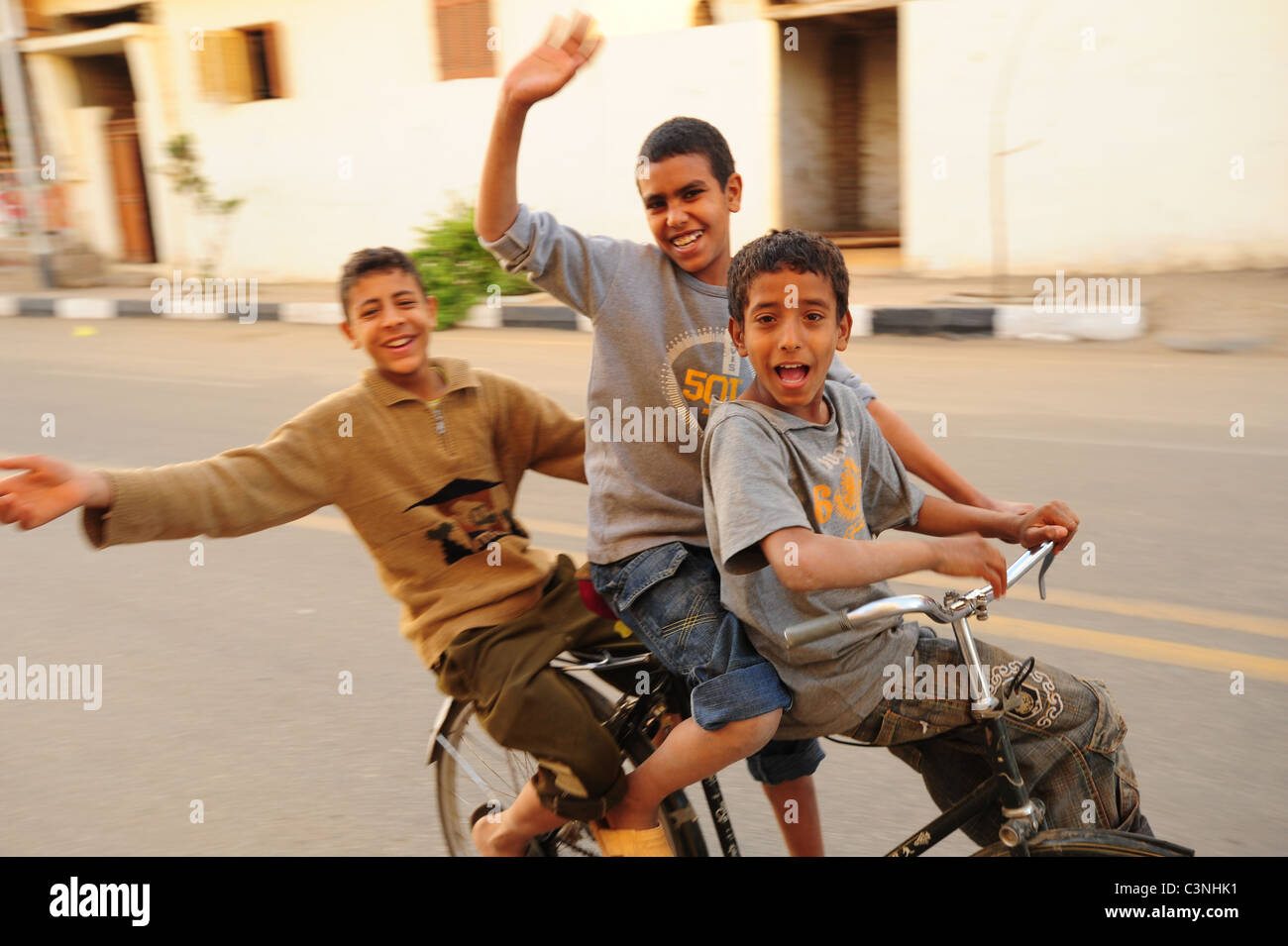 Africa Medio Oriente Egitto egiziani - tre ragazzi felice su una bicicletta su una strada di Luxor sventolando Foto Stock