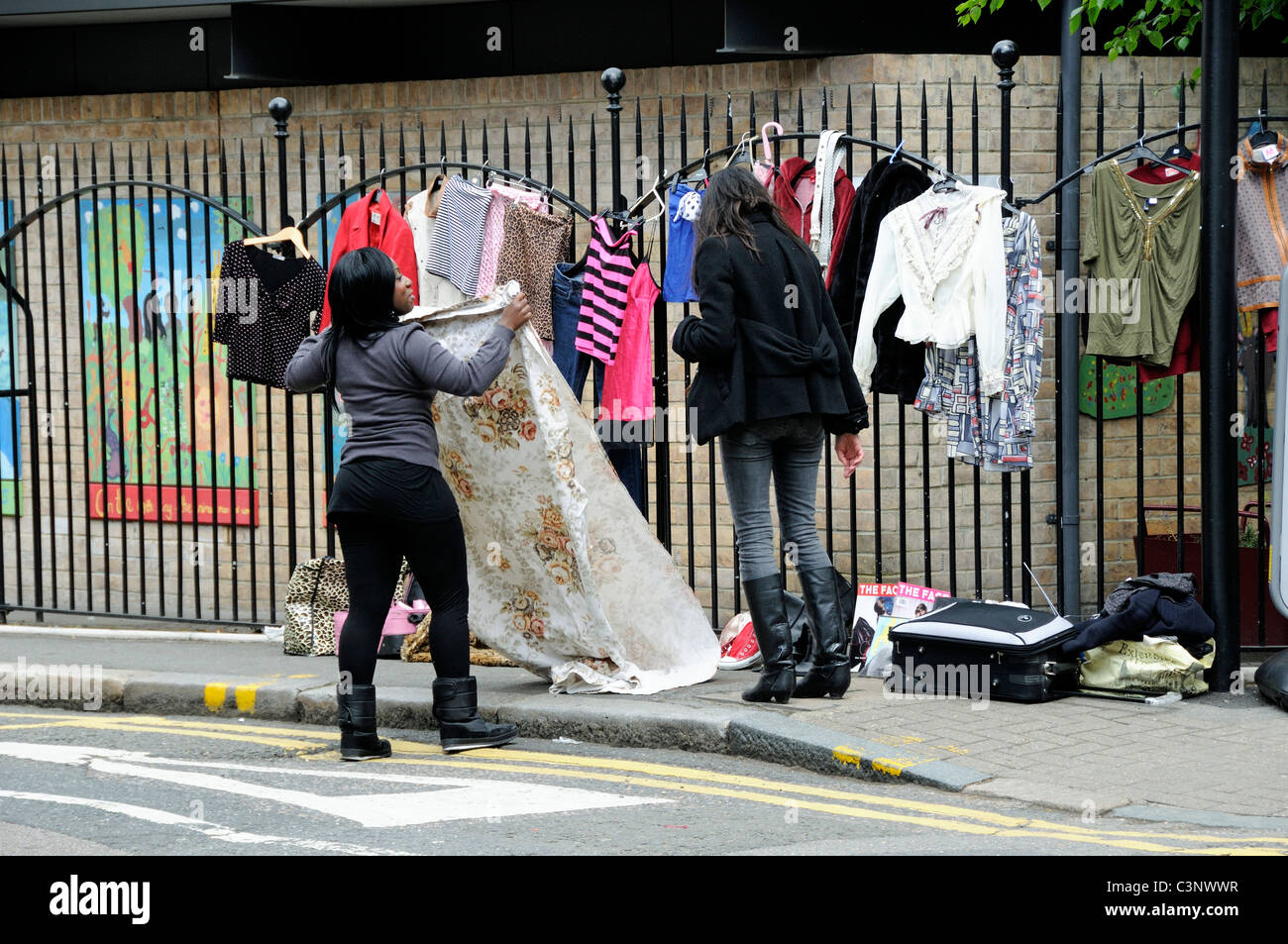Due donne che vendono vestiti per la strada utilizzando le ringhiere come appendiabiti Foto Stock
