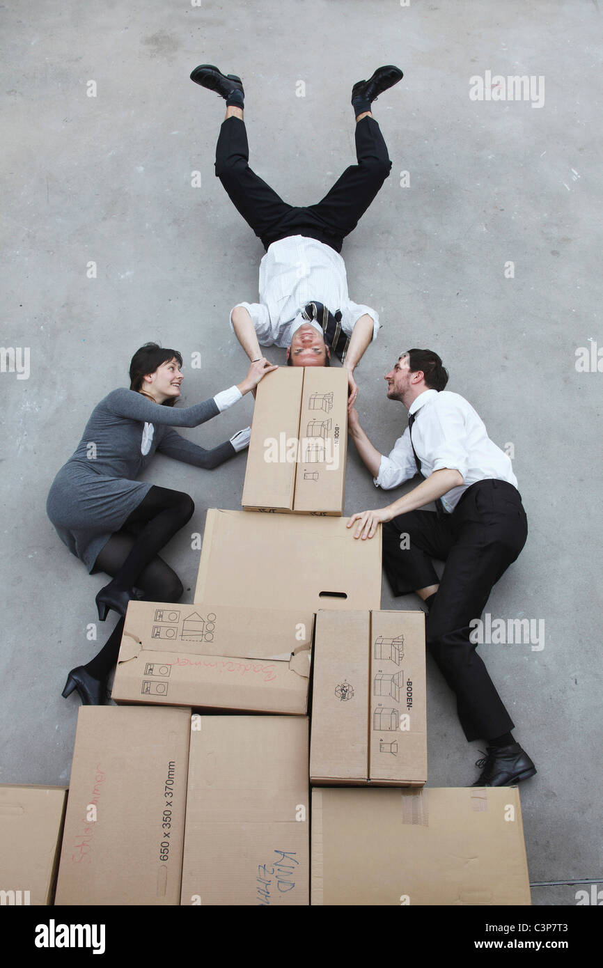 Tre persone di affari in scatole di cartone, uomo facendo handstand, sorridente, ritratto, vista in elevazione Foto Stock
