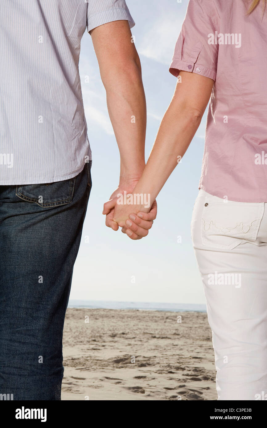 Germania, Schleswig Holstein, Amrum, giovane tenendo le mani sulla spiaggia, vista posteriore, metà sezione Foto Stock