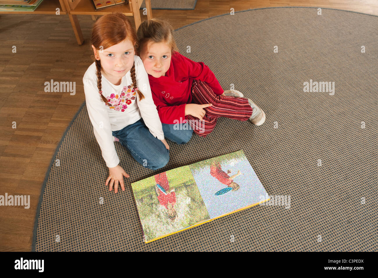 Germania, due ragazze (4-5), (6-7) in vivaio la lettura di un libro, ritratto, vista in elevazione Foto Stock