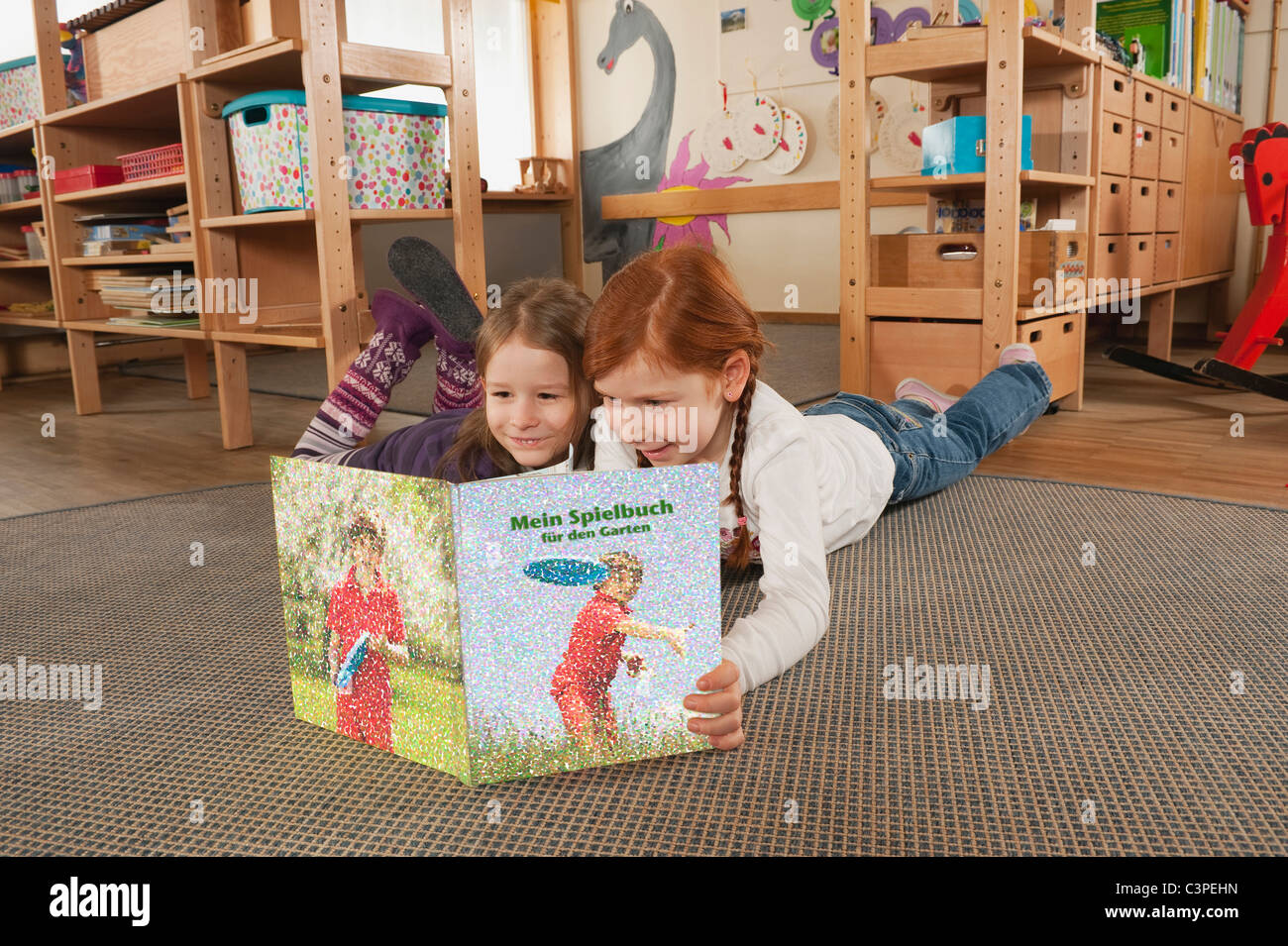 Germania, due ragazze (4-5), (6-7) in vivaio giacente su un tappeto o la lettura di un libro, ritratto Foto Stock
